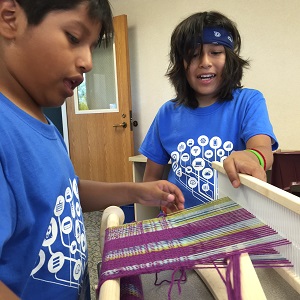 2 youth working on a loom