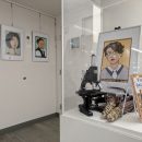 Framed illustrations of women in science on a wall, scientific research materials under an acrylic bonnet.