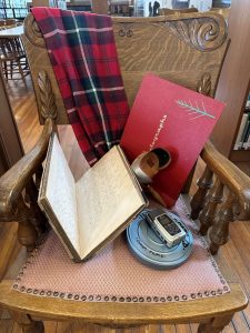 An old wooden chair with a variety of old items on it, including a canister of movie film, an old walkie talkie and a book with long hand writing.